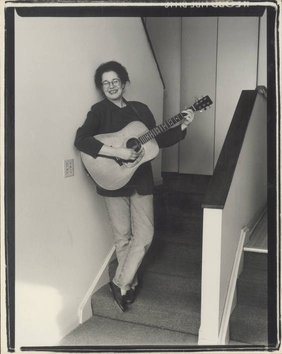 Katie Laur playing a guitar on a staircase