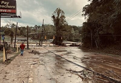 A flooded road with damaged traffic lights. A person and corner of a billboard are visible in the image.