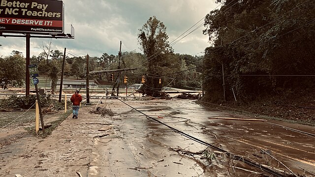 A flooded road with damaged traffic lights. A person and corner of a billboard are visible in the image.